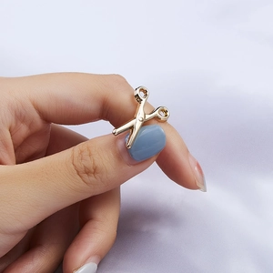 Detail of a small golden scissors pendant held by fingers to show compact size