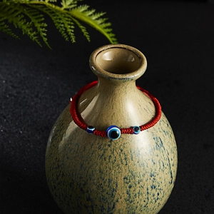 Detail of red woven cord bracelet with three blue evil eye beads on a ceramic vase