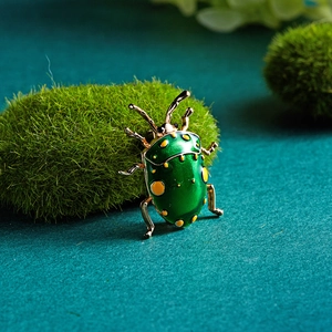 Macro shot of green enamel beetle brooch with gold metallic legs on mossy background