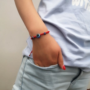 Detailed view of hand-woven red string bracelet with three blue Evil Eye beads on a wrist