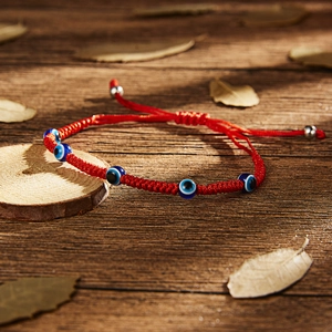 Detailed view of handmade red string woven bracelet with five blue evil eye charms