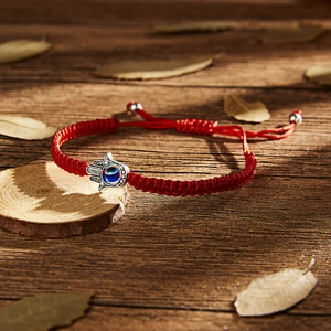 Detailed view of red woven Evil Eye bracelet with Hamsa Hand charm on a rustic wood base