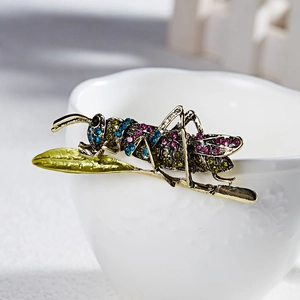 Exquisite grasshopper brooch with colorful rhinestones on a green leaf base