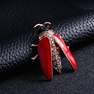 Detailed close-up of a red enamel beetle brooch with crystal rhinestones on black leather