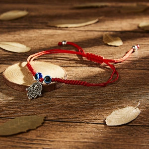 Detail of red woven string bracelet with Hamsa hand and evil eye charms on wood