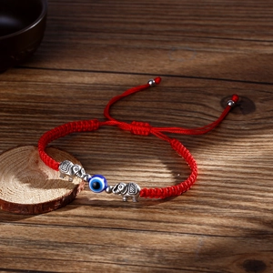 Red braided cord bracelet with silver elephant charms and a blue evil eye bead on wood