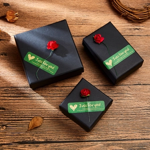 Three elegant black gift boxes with red paper roses and greeting stickers on wood surface