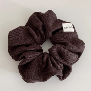 Detail of dark brown knitted scrunchie showing hand made label and thick fabric texture