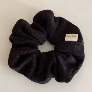 Detail of black ribbed knit scrunchie featuring a white Hand Made woven label