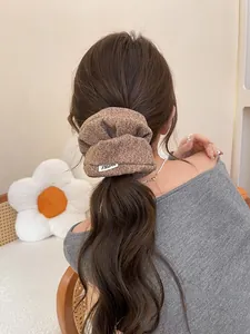 Détail d'un chouchou en tweed marron sur cheveux ondulés avec une étiquette élégante
