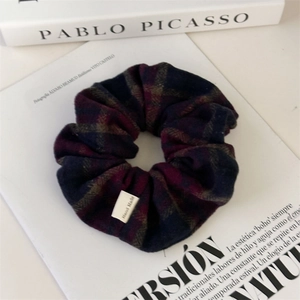 Detail view of plaid scrunchie with Hand Made label beside art books in a retro style