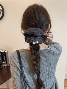 Détail d'un chouchou en maille gris foncé avec étiquette FMdrea sur une tresse souple