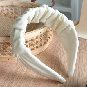 Detailed view of the layered pleats on this cream white wide headband on a rustic background