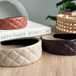 Close-up of quilted faux leather headbands in beige, brown and red on a rustic wooden desk