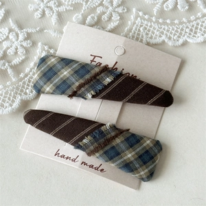 Detailed view of handmade plaid fabric hair clips with fringe on a display card