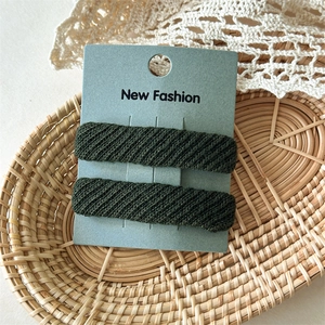 Close-up of dark green twill fabric hair clips with woven texture on display card