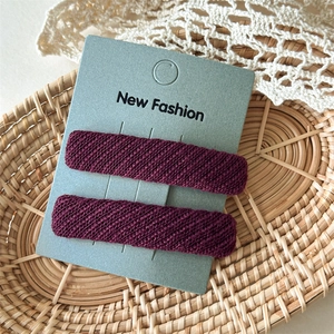 Detail of two burgundy twill fabric hair clips displayed on a card in a soft woven basket