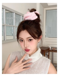 Detail view of large pink plush hair scrunchie styled on a woman's bun hairstyle