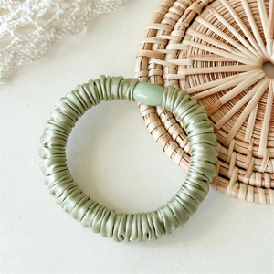 Détail d'un chouchou en satin vert avec texture plissée et ornement en perle ovale
