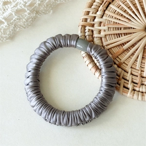 Détail d'un chouchou en satin gris avec texture plissée et boucle en résine lisse