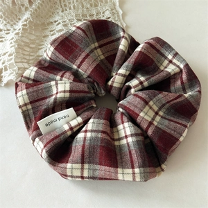 Detailed close-up of dark red plaid hair scrunchie with handmade fabric label