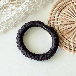 Détail d'un chouchou en satin noir avec texture plissée et boucle de connexion brillante
