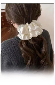 Detailed view of an ivory satin scrunchie with embossed patterns on brown wavy hair
