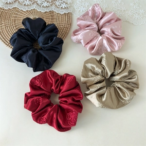 Detailed macro view of four satin scrunchies with embossed rose patterns in multiple colors