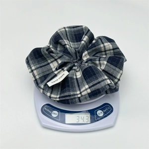 Detail view of a vintage navy plaid scrunchie with a handmade tag on a scale