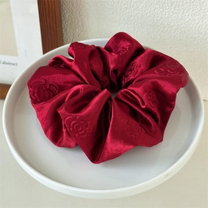 Detail shot of a burgundy embossed satin scrunchie with floral patterns on a ceramic tray