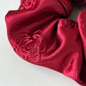 Macro shot of red satin scrunchie with embossed rose floral texture and silk sheen