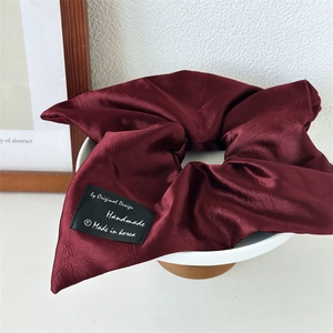 Deep burgundy satin scrunchie with silky luster and handmade label on white tray