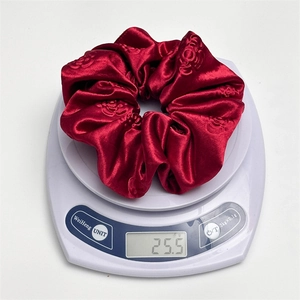 Deep red satin scrunchie with floral embossing weighing 25.5g on a digital scale