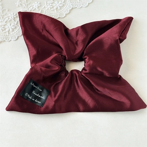 Close-up of wine red oversized silk scrunchie with handmade tag on white lace backdrop