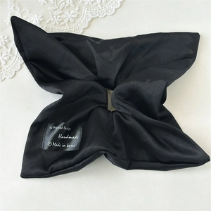 Close-up of black satin hair scrunchie showing glossy texture and handmade label details