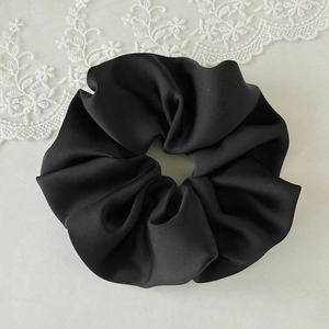 Detailed close-up of a large black satin scrunchie with soft silk texture and pleated folds