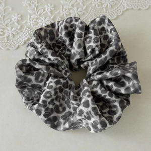 Detail of leopard print satin scrunchie showing smooth texture and elegant pleats