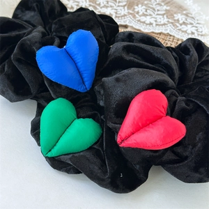 Détail d'un chouchou en velours noir avec des breloques en forme de cœur bleu, vert et rouge