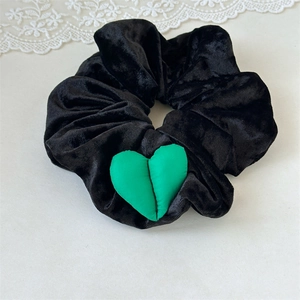 Détail d'un chouchou en velours noir orné d'un pendentif en forme de cœur vert