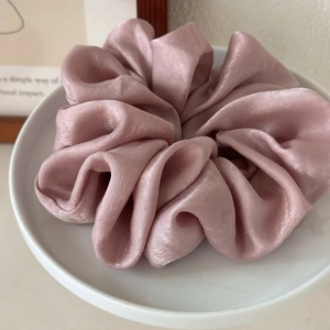 Close-up of pink satin scrunchie with silky sheen and pleated texture on white tray