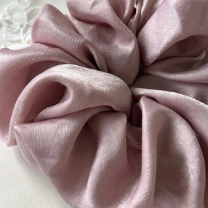 Close-up of thick satin scrunchie in dusty rose with smooth silky texture and soft folds
