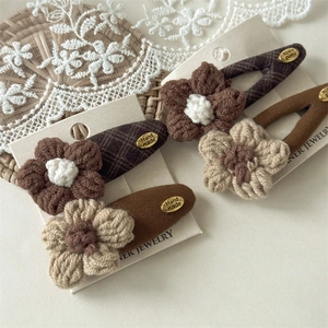 Detail of knitted flower hair clips with handmade gold labels on lace and rattan