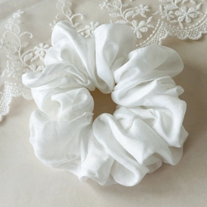 Macro shot of white satin scrunchie with silky folds and elegant lace background