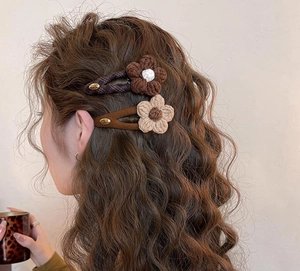 Detailed close-up of knitted flower hair clips styled on wavy brown hair for autumn look