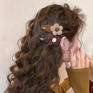 Detail of wool knit flower hair clips in brown and beige on wavy brunette hair