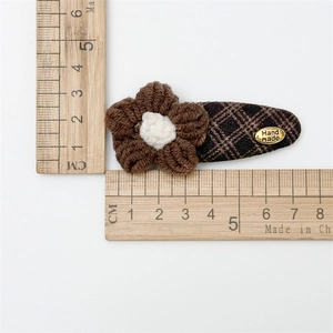 Detail view of a vintage knitted flower hair clip with a gold handmade tag and brown check