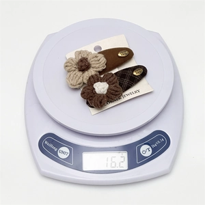 Detail showing weight of 16.2g for two handmade knitted flower hair clips on a scale