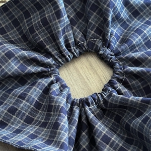 Close-up of blue and grey checkered fabric scrunchie with detailed stitching on wood background