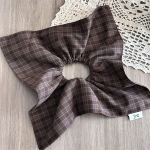 Detail of brown plaid scrunchie with ruffled edges and small bow label on wood background