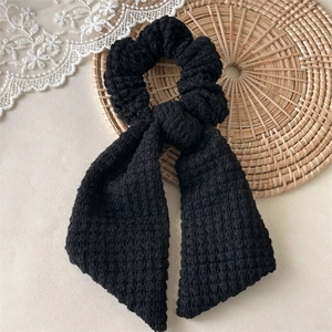 Detail of black handmade crochet scrunchie with long bow on a woven mat surface